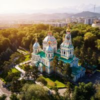aerial-drone-panorama-of-the-ascension-cathedral-russian-orthodox-church-and-snow-mountains-at-background-in-panfilov-park-at-glow-sunrise-light-in-almaty-city,-kazakhstan